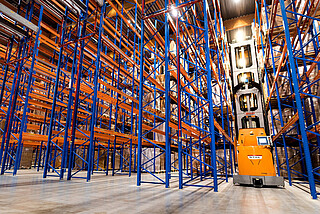 Wózek systemowy VNA STILL MX-X wśród regałów wysokiego składowania.